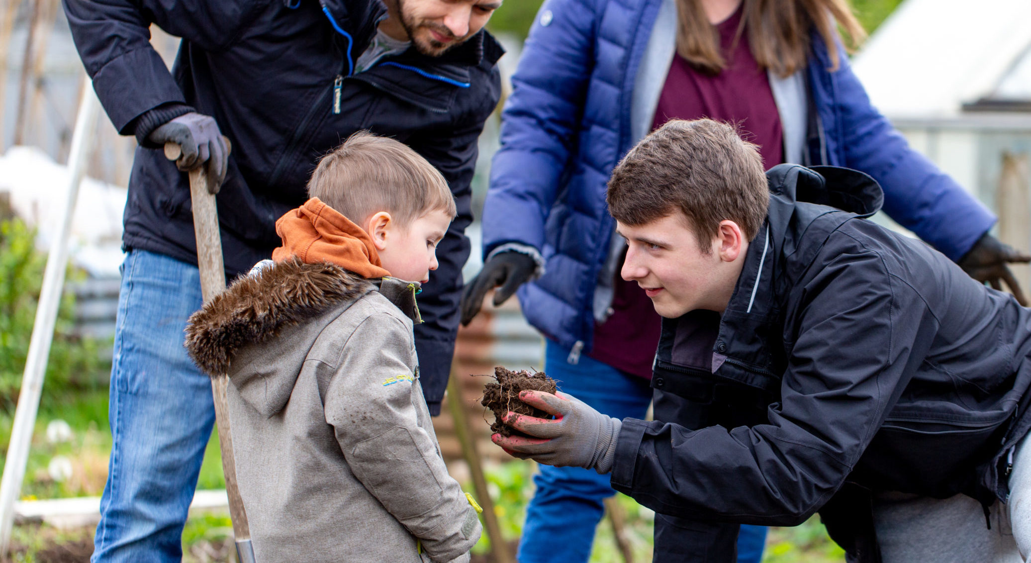 Teenage boy helping younger boy with gardening, holding soil