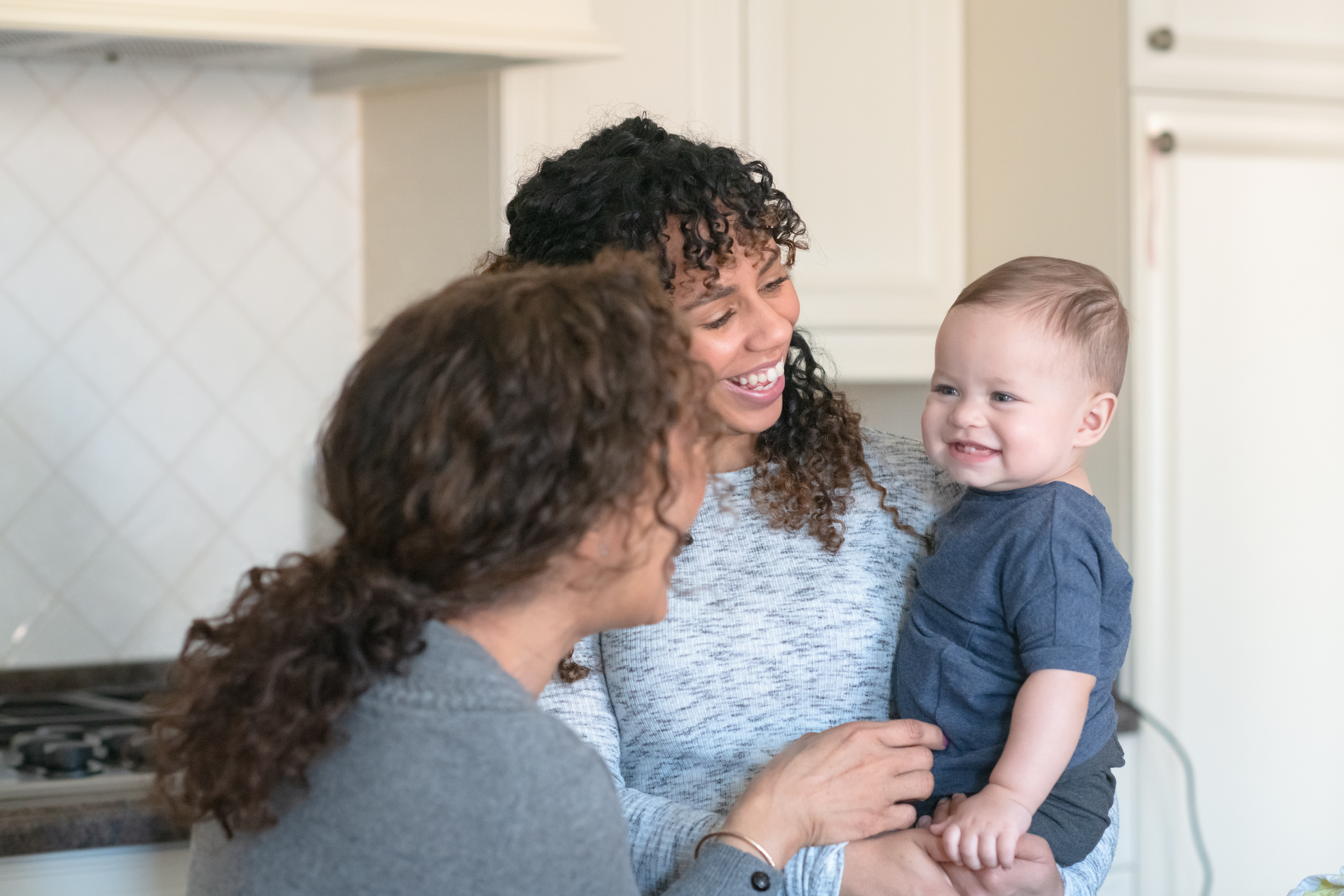 two women smiling at toddler in kitchen